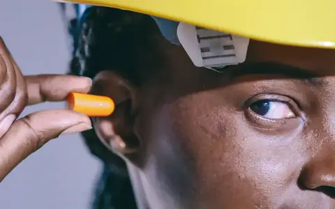Lavoratrice con elmetto inserisce un inserto auricolare