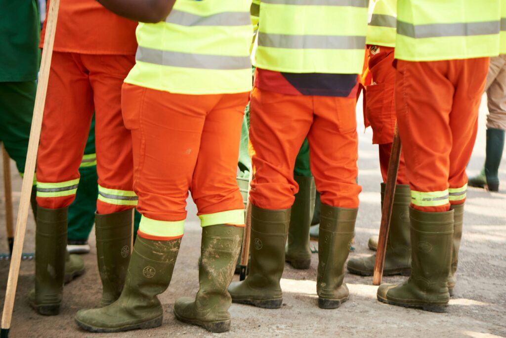 Group of construction workers wearing high visibility gear and boots standing outdoors.