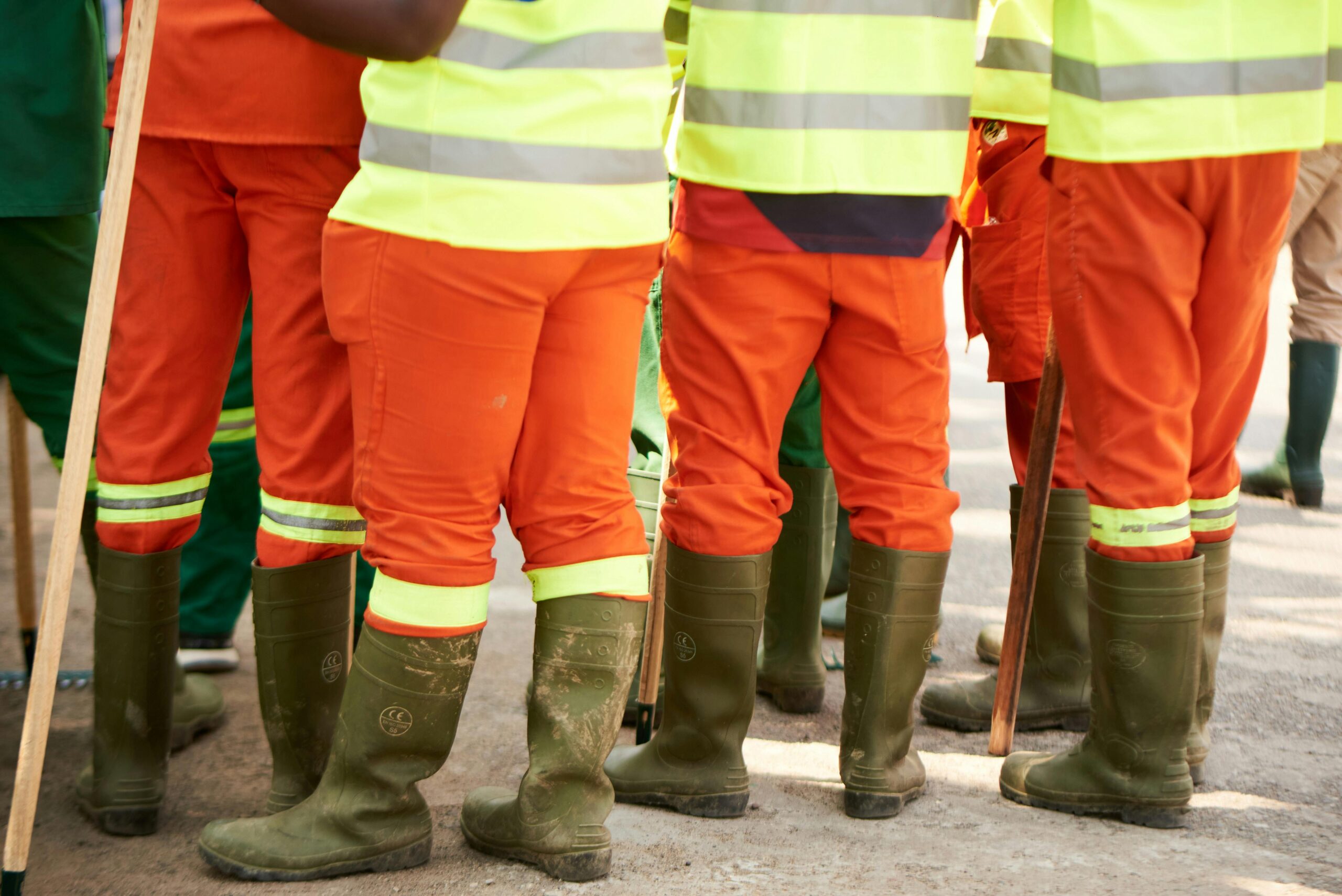 Group of construction workers wearing high visibility gear and boots standing outdoors.