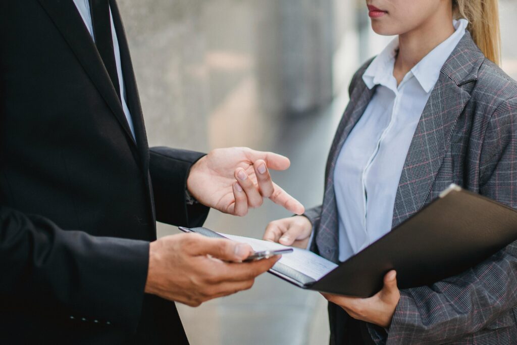 A businessman and businesswoman in formal attire engage in a focused discussion outdoors.