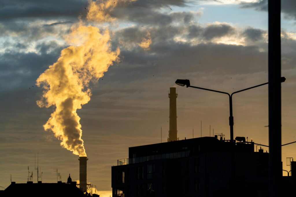 Silhouette of a factory chimney emitting smoke against a sunset sky, highlighting air pollution.