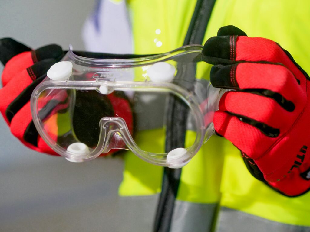 Close-up image of a person holding safety goggles with protective gloves, emphasizing PPE.