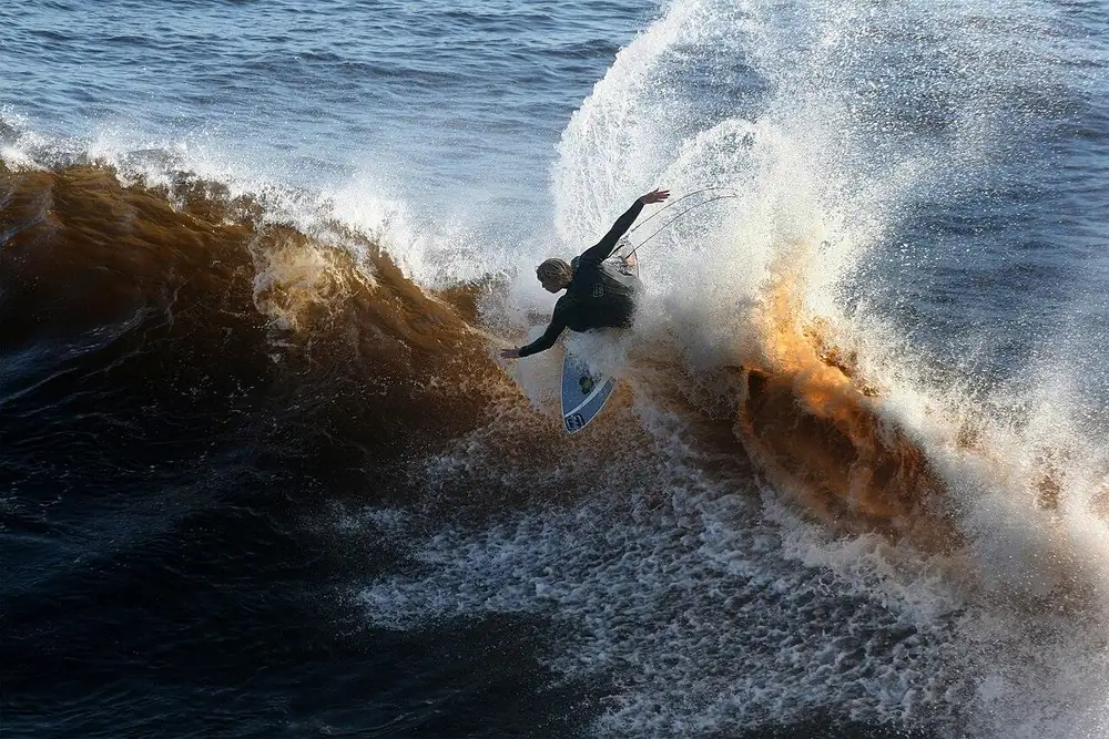 Surfista in azione sulla cresta di un’onda, tra spruzzi controluce
