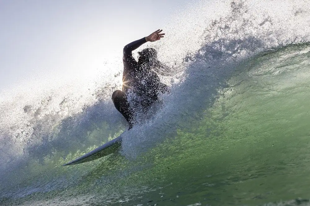 Surfista che taglia l’onda sollevando un’ala di spruzzi